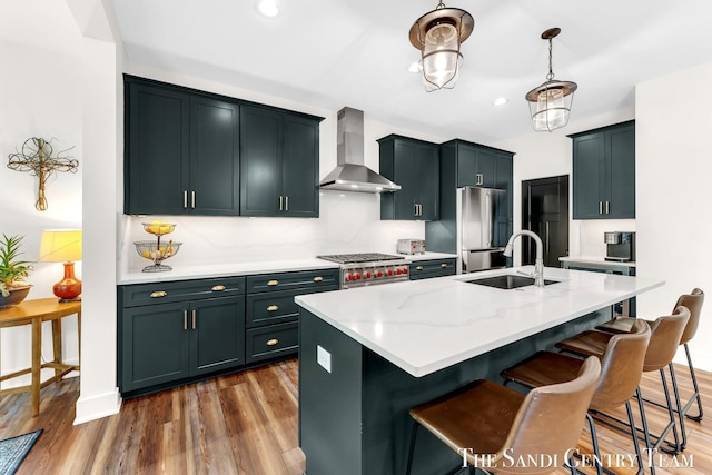 kitchen with a sink, wall chimney exhaust hood, stainless steel appliances, wood finished floors, and a kitchen breakfast bar