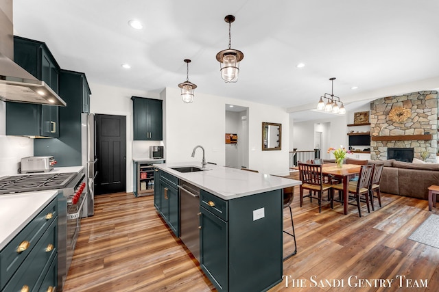kitchen featuring a sink, stainless steel appliances, wall chimney exhaust hood, light wood finished floors, and light countertops