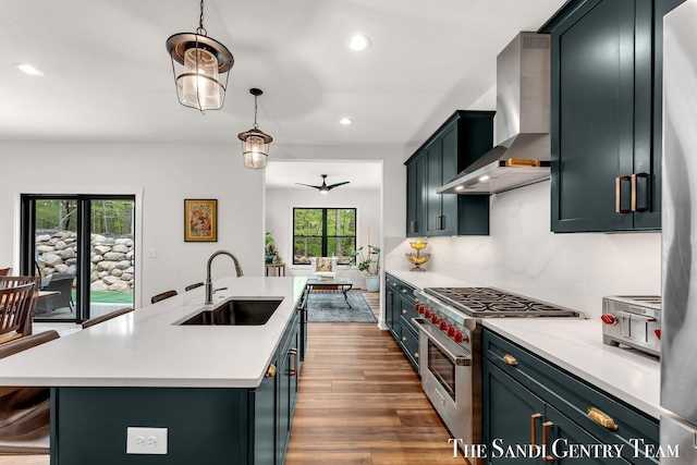 kitchen featuring high end stainless steel range, a sink, wall chimney exhaust hood, light countertops, and recessed lighting