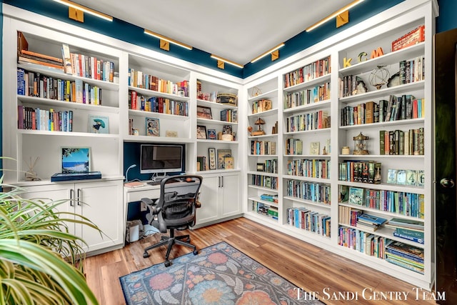 office area featuring wall of books, built in study area, and light wood-type flooring