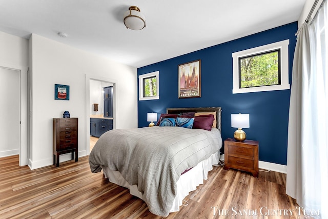 bedroom with light wood-style flooring, baseboards, and connected bathroom