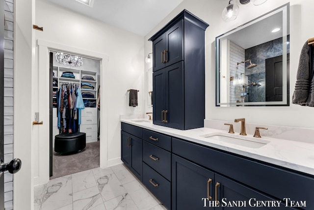 bathroom featuring marble look tiles, a tile shower, double vanity, a walk in closet, and baseboards