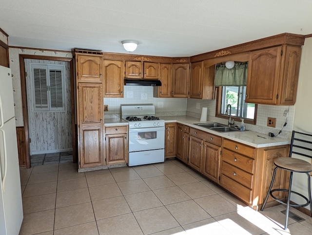 602 Fourth St, Ludington, MI 49431 - kitchen featuring a sink, white appliances, under cabinet range hood, brown cabinets, and decorative backsplash