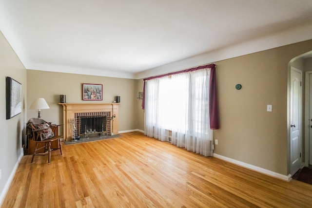 unfurnished living room featuring a brick fireplace, arched walkways, light wood finished floors, and baseboards
