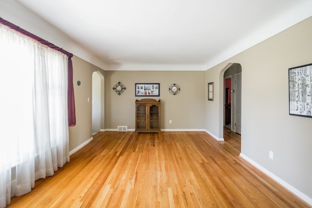 unfurnished living room featuring arched walkways, light wood-type flooring, and baseboards