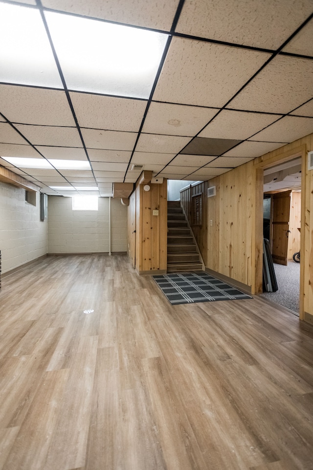 below grade area with wood finished floors, stairs, a drop ceiling, and wood walls