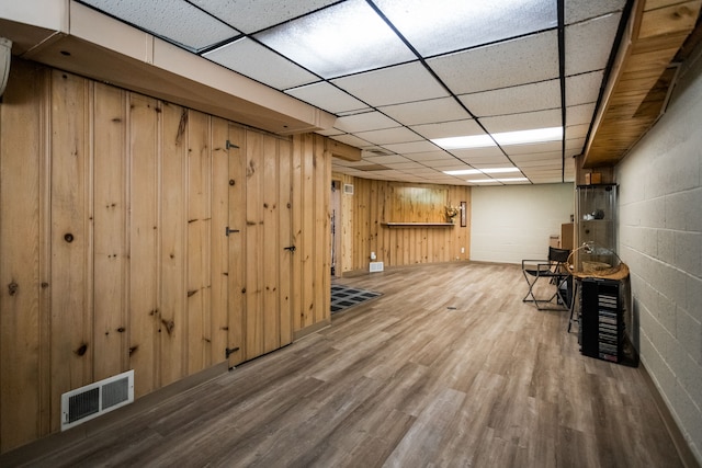 unfurnished room featuring wood finished floors, wooden walls, a drop ceiling, and concrete block wall