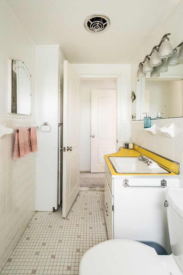 half bath featuring tile walls, toilet, tile patterned floors, and vanity
