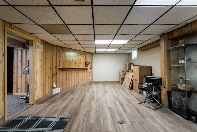 basement with wood finished floors, wooden walls, and a drop ceiling