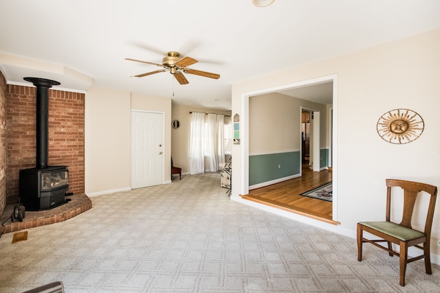unfurnished living room featuring a wood stove, ceiling fan, carpet floors, and baseboards