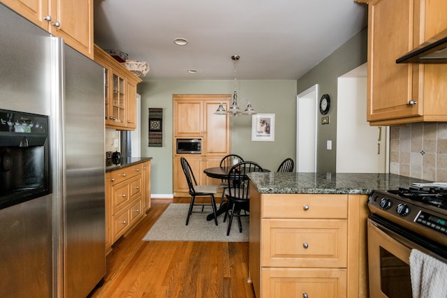 kitchen featuring stainless steel appliances, wall chimney range hood, dark wood finished floors, backsplash, and a chandelier