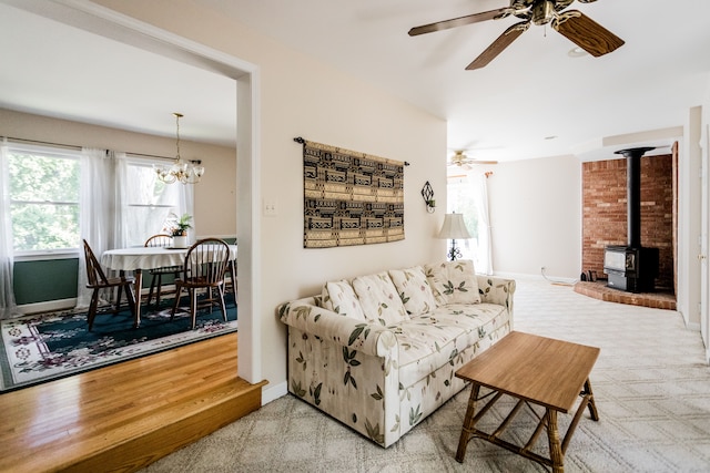 carpeted living room featuring a wood stove, a ceiling fan, baseboards, and a chandelier