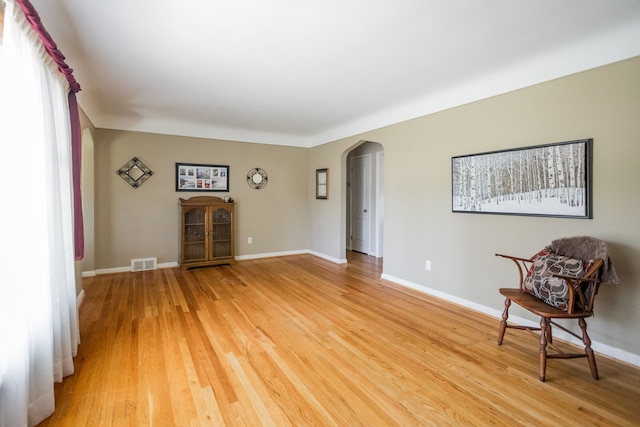 living area with arched walkways, light wood-style floors, and baseboards