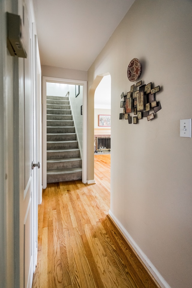 corridor featuring arched walkways, light wood finished floors, stairway, and baseboards