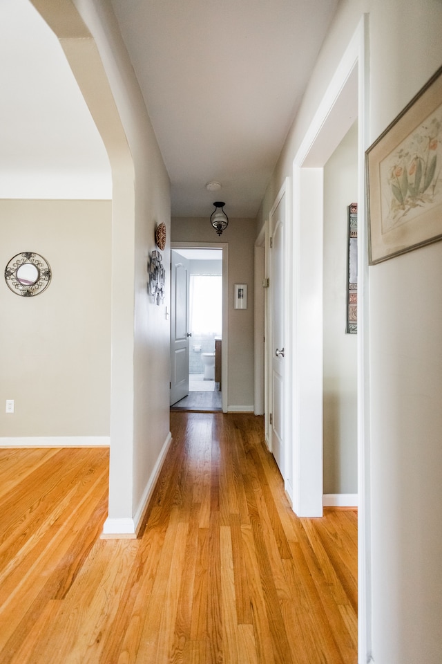 hallway featuring light wood-style floors, baseboards, and arched walkways