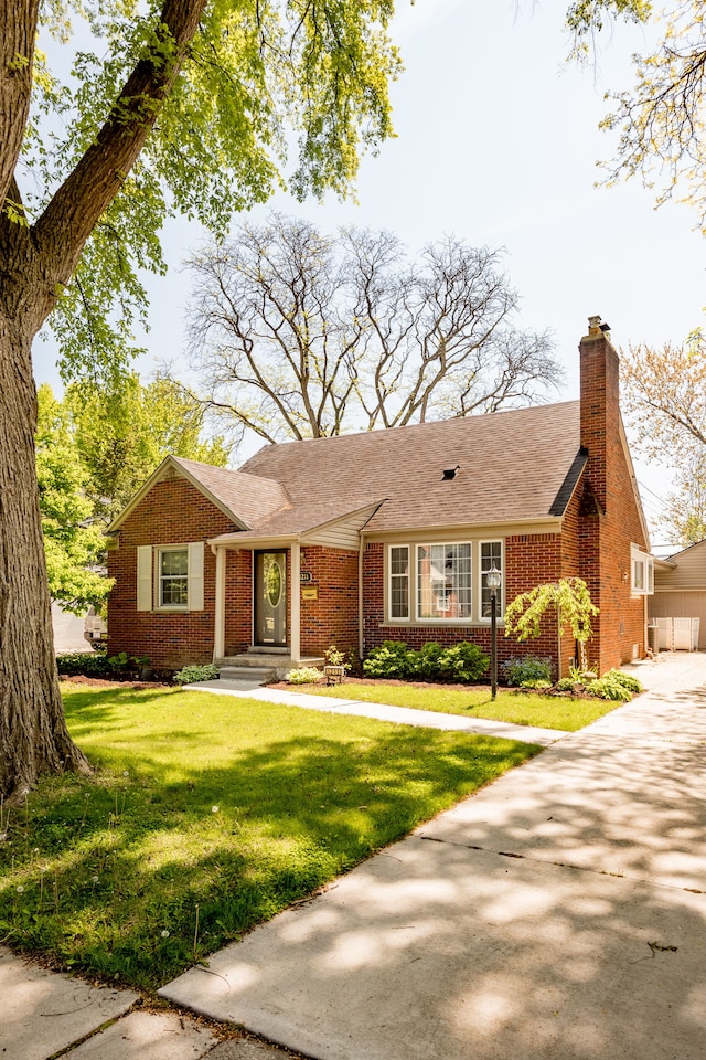 single story home featuring brick siding, a front yard, a chimney, and a shingled roof
