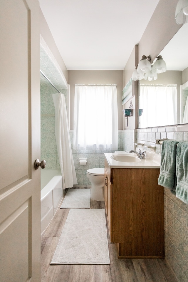 bathroom with tile walls, vanity, wood finished floors, toilet, and shower / bath combo with shower curtain