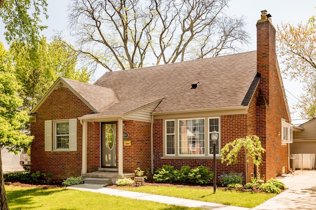 view of front of property with brick siding, a chimney, a front yard, and a shingled roof