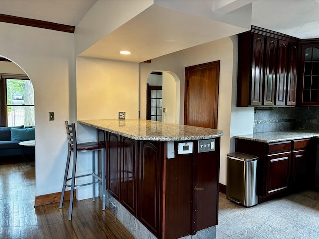 404 Pauline Blvd, Ann Arbor, MI 48103 - kitchen featuring arched walkways, a kitchen bar, glass insert cabinets, light stone countertops, and backsplash