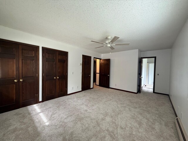 6035 W Trails End Rd, Ludington, MI 49431 - unfurnished bedroom featuring a baseboard radiator, light carpet, multiple closets, baseboards, and a textured ceiling