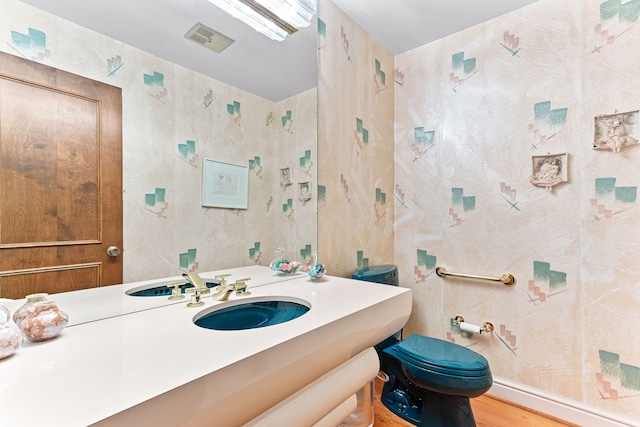 bathroom with wood finished floors, wallpapered walls, toilet, and vanity