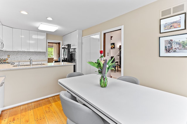 kitchen featuring a sink, light wood-style floors, white cabinetry, light countertops, and decorative backsplash