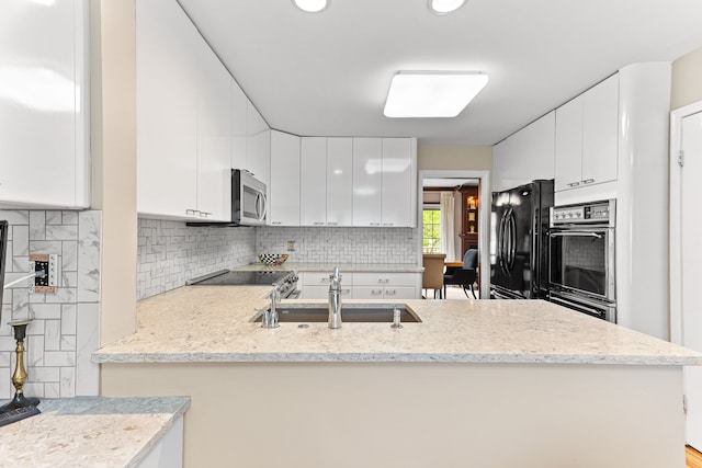 kitchen with a sink, backsplash, appliances with stainless steel finishes, white cabinets, and a peninsula