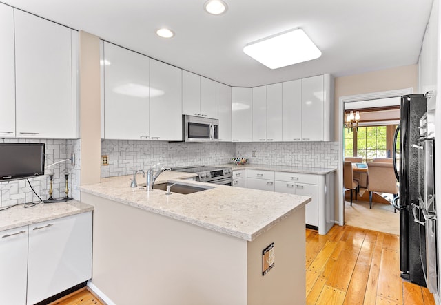 kitchen with stainless steel appliances, a sink, light wood finished floors, a peninsula, and recessed lighting