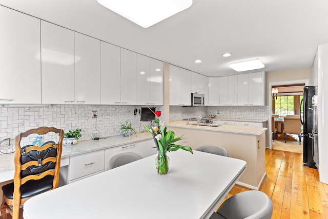 kitchen with stainless steel microwave, white cabinetry, backsplash, a breakfast bar, and a sink