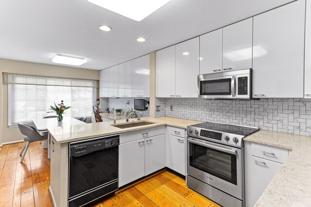 kitchen with appliances with stainless steel finishes, a sink, white cabinets, light wood finished floors, and a peninsula
