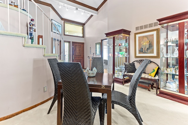 carpeted dining area featuring crown molding, a high ceiling, baseboards, and rail lighting