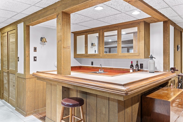 indoor wet bar with a paneled ceiling, a wainscoted wall, and light tile patterned floors