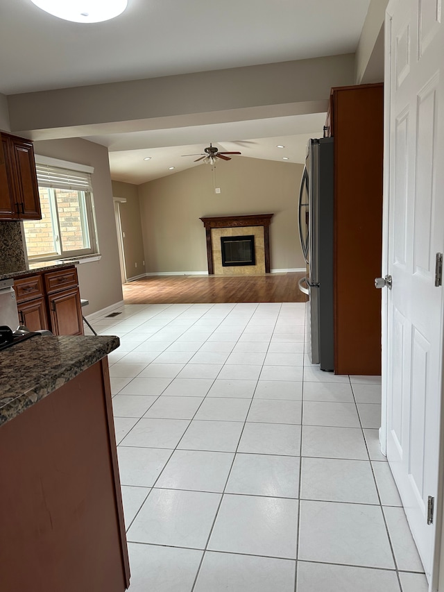 kitchen with freestanding refrigerator, a ceiling fan, light tile patterned floors, open floor plan, and a glass covered fireplace