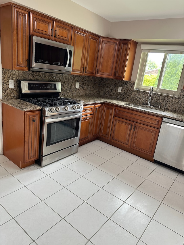 kitchen featuring appliances with stainless steel finishes, a sink, decorative backsplash, brown cabinetry, and light tile patterned floors