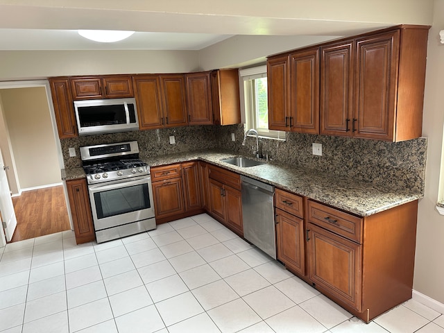 kitchen with appliances with stainless steel finishes, a sink, decorative backsplash, and brown cabinets