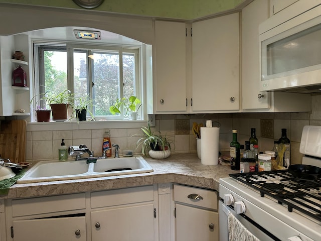 kitchen with white appliances, a sink, white cabinets, and decorative backsplash