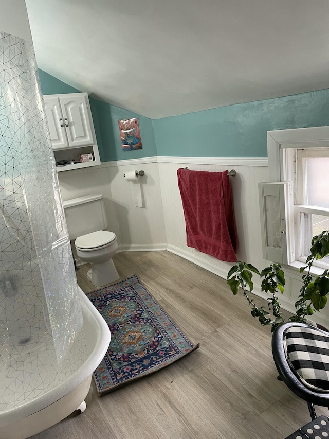 bathroom with wainscoting, wood finished floors, lofted ceiling, toilet, and curtained shower
