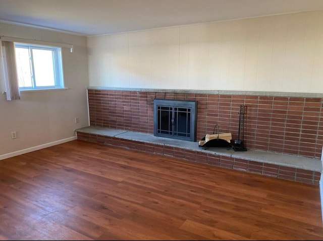 unfurnished living room featuring wood finished floors, a brick fireplace, and baseboards