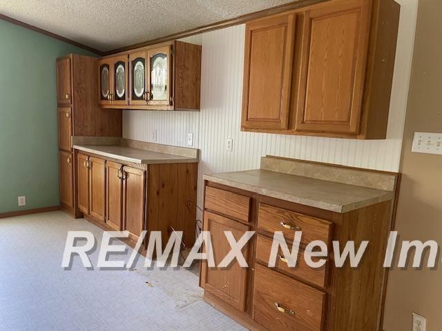 1944 S M 18 Hwy, Gladwin, MI 48624 - kitchen with brown cabinets, a textured ceiling, glass insert cabinets, baseboards, and crown molding