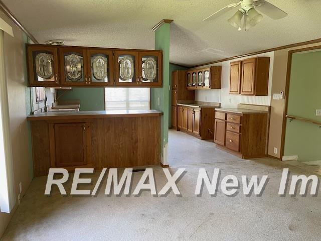 1944 S M 18 Hwy, Gladwin, MI 48624 - kitchen featuring brown cabinets, a ceiling fan, light carpet, glass insert cabinets, and a peninsula
