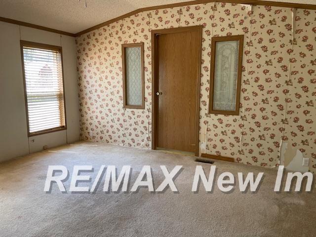 1944 S M 18 Hwy, Gladwin, MI 48624 - empty room featuring ornamental molding, wallpapered walls, a textured ceiling, carpet, and lofted ceiling