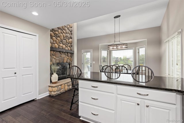4470 Coastal Pkwy, White Lake, MI 48386 - kitchen featuring a breakfast bar area, white cabinetry, dark wood-style floors, pendant lighting, and a fireplace