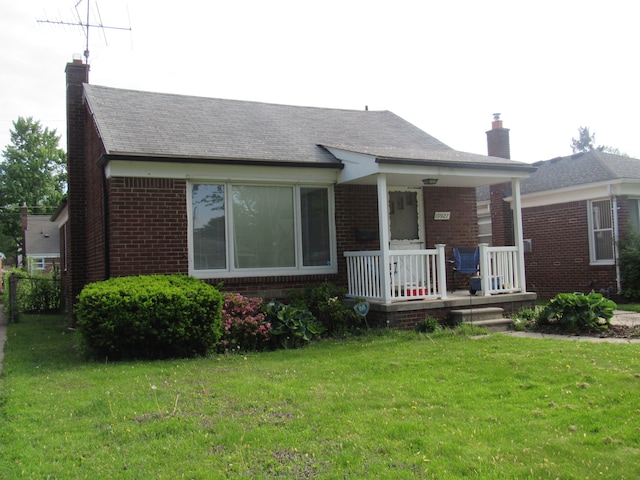 view of front facade featuring a chimney, a porch, brick siding, and a front lawn