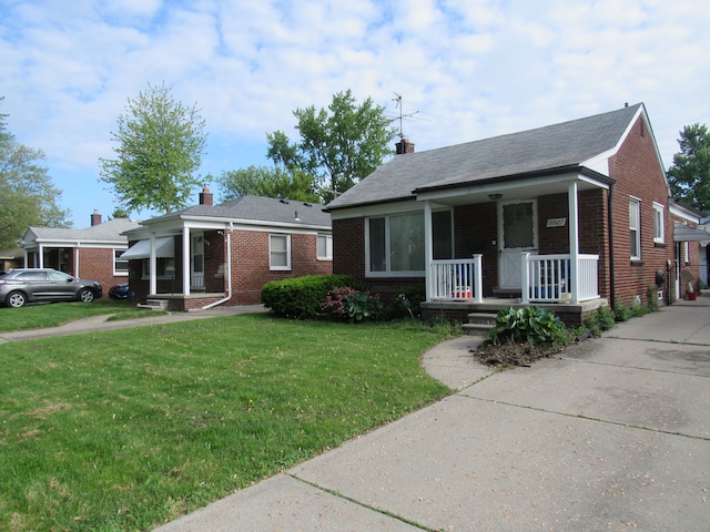 view of front of home with covered porch, brick siding, a front yard, and a chimney