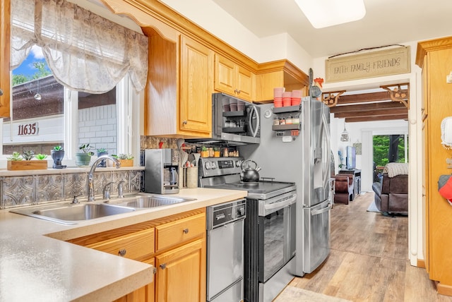 kitchen with stainless steel appliances, a sink, light wood finished floors, light countertops, and light brown cabinets