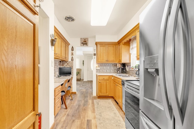 kitchen with stainless steel appliances, a sink, light countertops, light wood-style floors, and decorative backsplash