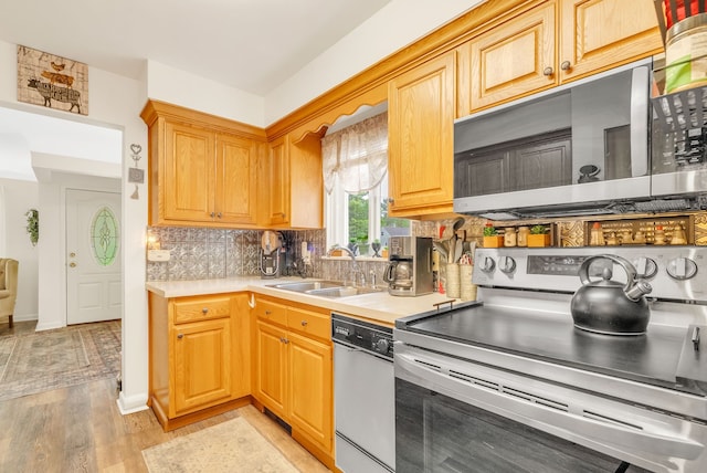 kitchen with appliances with stainless steel finishes, a sink, light countertops, and decorative backsplash