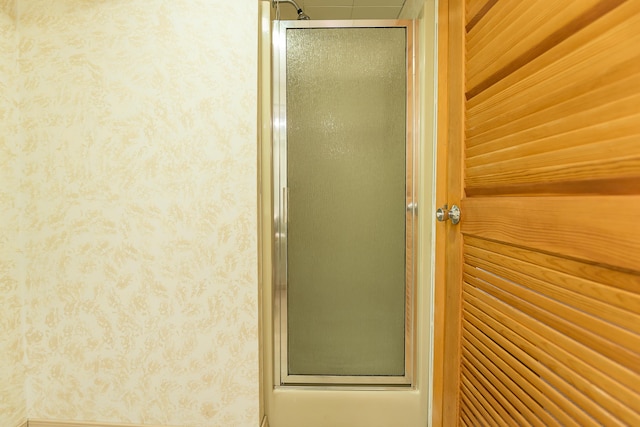 bathroom featuring a shower with shower door and wallpapered walls