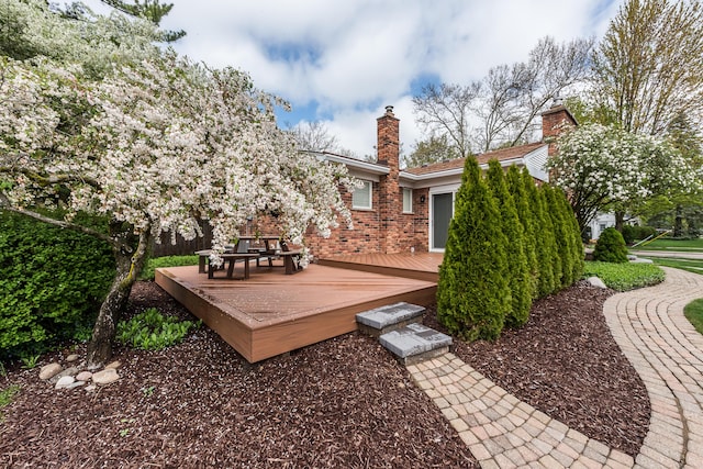back of house featuring a wooden deck, a chimney, and brick siding