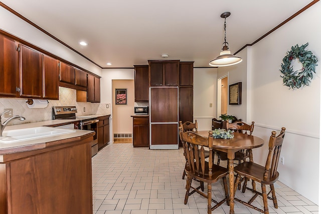 kitchen featuring built in appliances, a sink, backsplash, crown molding, and decorative light fixtures